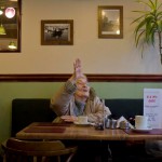 Barbara from the Drive in Deco community participation film project sits in a cafe and waves cheerfully out of the window